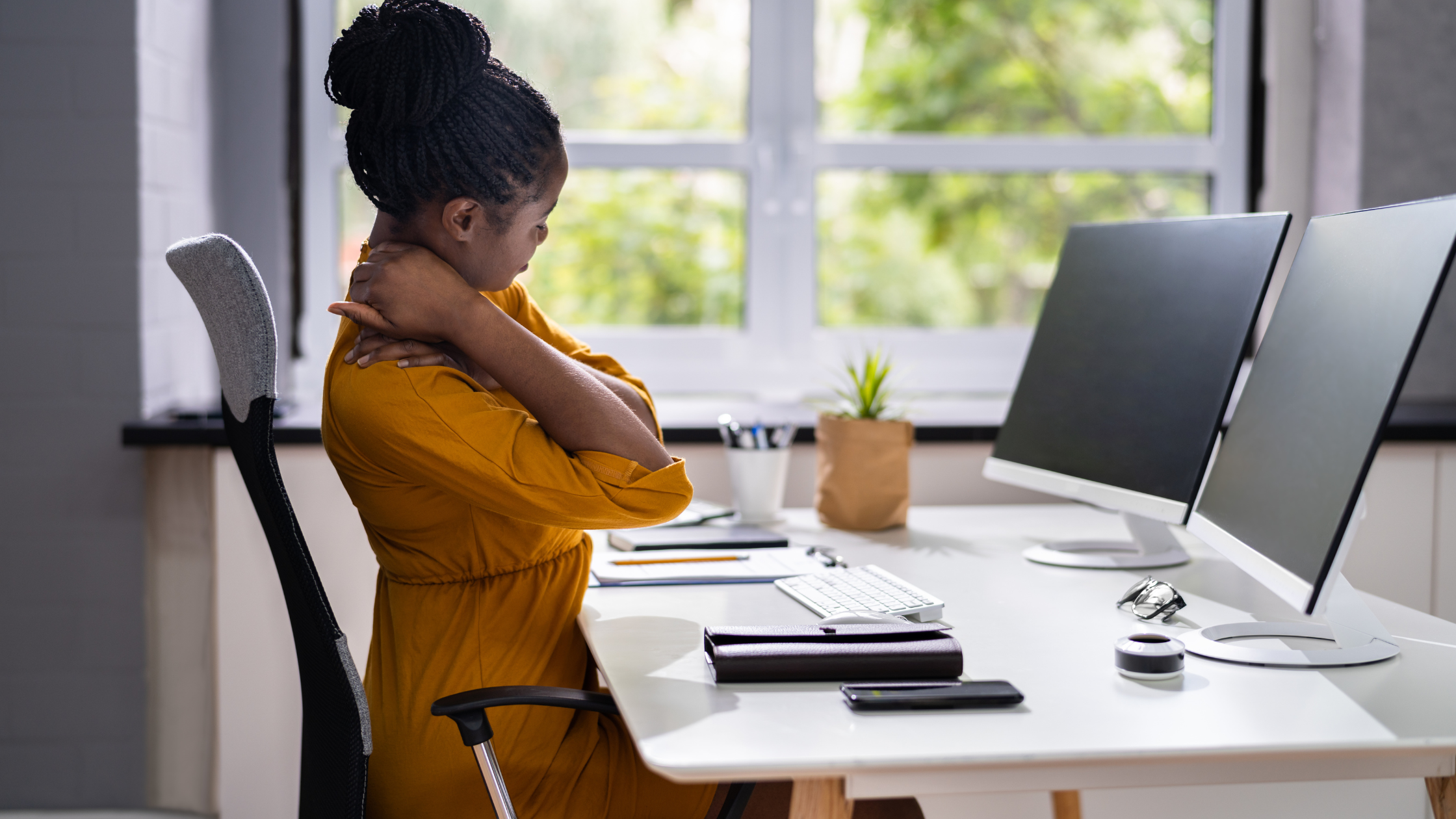 Business woman sits at desk stretching her neck