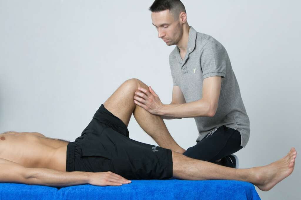 Sports medicine doctor examining patient leg demonstrating treatment and rehabilitation techniques