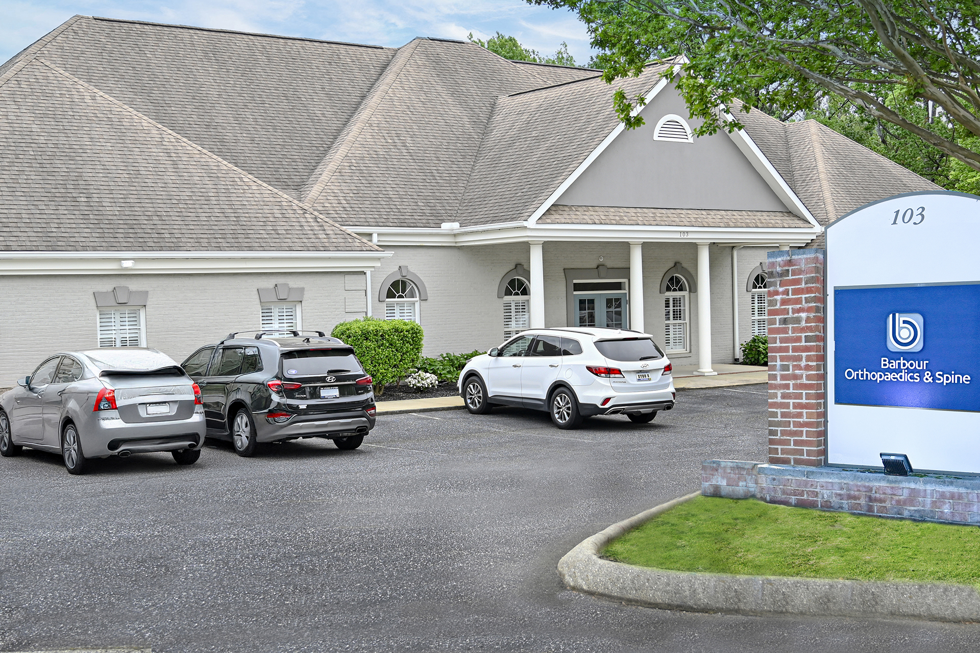 Exterior of Barbour Orthopaedics & Spine clinic at 103, with a blue sign and several parked cars in front.