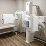 Hospital X-ray machine in a clean imaging room with a patient table and control panel nearby