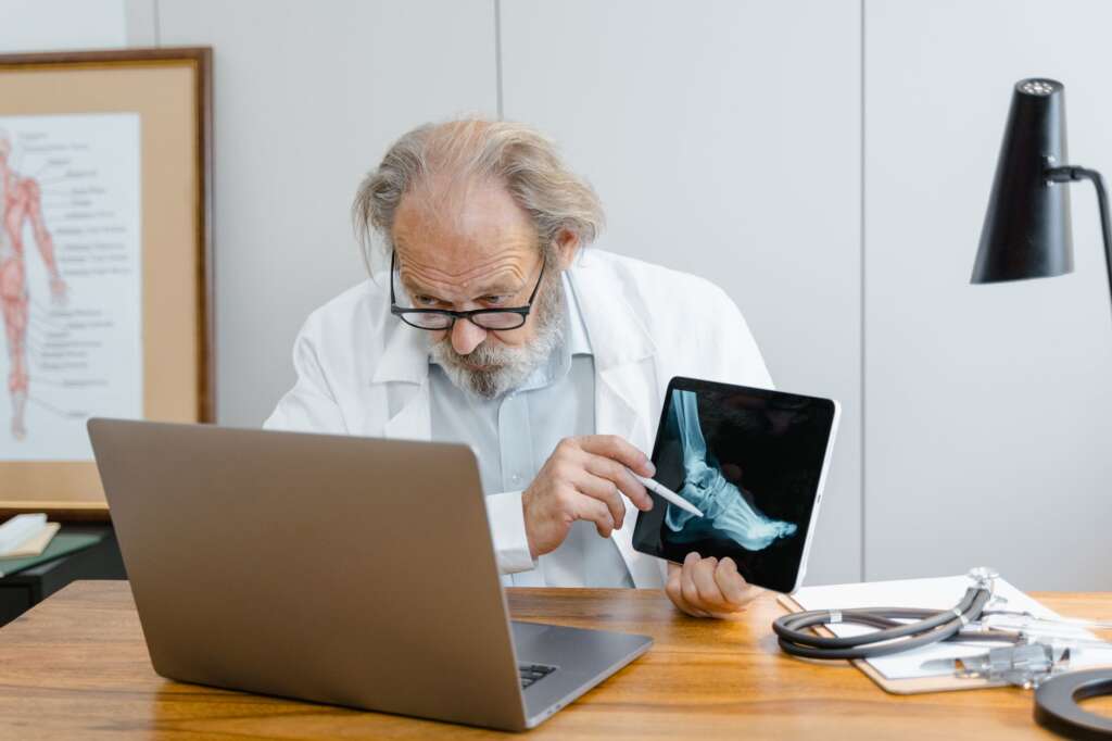 Senior sports medicine doctor reviewing a foot and ankle X-ray on a tablet in a medical office